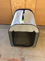 Front view of the portable dog crate showing mesh door, carry handle and tag on top.