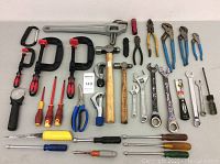 Photo showing entire assortment of hand tools laid out on a white surface, including clamps, wrenches, hammers, pliers, scissors and screwdrivers.