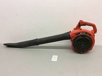 Side view of the entire gas powered leaf blower showing the red body and black nozzle.