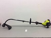 Side profile view of entire Ryobi gas powered weed wacker showing shaft, handle, and cutting head with guard.