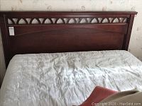 Front view of wooden bed frame headboard with mattress covered by white quilted cover.