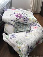 Folded white quilt with large floral patterns and a smaller folded blue fabric item on top.