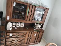 Overall view of the wooden buffet and hutch showing upper glass cabinets filled with glassware and lower drawers and cabinets with ceramic containers on top.