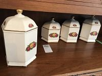 Front view of the set of four ceramic canisters arranged by height on a wooden surface, showing lids with gold-tone finials, and floral designs.