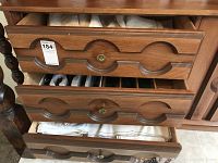 Wooden cabinet with multiple drawers, some open showing folded table linens and flatware