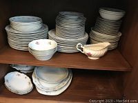 Shelved fine china plates, multiple stacks including plates and bowls, decorations in floral and gold trim, and a gravy boat with floral pattern.