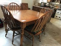 Wide view of entire dining table with six chairs around it showing wood finish and chair cushions.