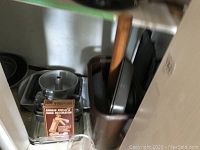 Shelve with stacked metal loaf pans, dark rectangular casserole dish upright with wooden rolling pin inside, and boxed cookie press visible.