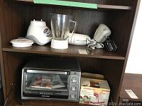 Overall view of shelf with Black & Decker toaster oven, Osterizer blender, Starfrit apple peeler box, Procter Silex and Hamilton Beach hand blenders/mixers.