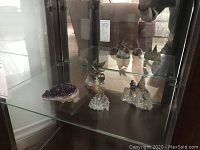 Crystal decor pieces including amethyst and quartz clusters with metal bird sculptures inside a glass cabinet.
