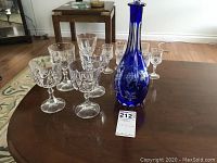Full view of the lot showing the cobalt blue decanter with stopper and assorted crystal stemware on a wooden table.