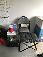 Photo showing folding chair, two black folding stools, and some coolers stacked next to wall.