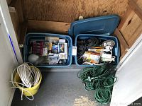 Full lot view showing two large blue containers and a yellow bucket filled with extension cords, cables, and light bulbs