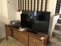 RCA 40 inch LED TV on wooden stand next to staircase, showing full screen and remote controls on stand