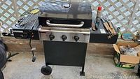 Master Chef black metal gas grill with three burner knobs, side tables, grill lid with thermometer, and grilling tools arranged on sides.