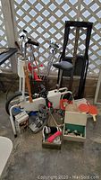 Wide view of the lot showing York Alpine Tracker stationary exercise bike, golf clubs in bag, golf balls, badminton rackets, shoe shine kit, tensor bandage, and arm blood pressure tester.