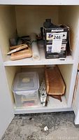Photo of shelving unit with painting supplies, a box with the Mastercraft sheet sander, paint brushes, plastic wrap, staple gun, miter box and saw on shelves.