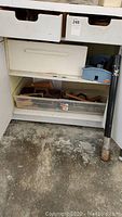 Open cabinet showing plastic box with small tools including hand planer parts or wood shavings, a grey box, and long handled wooden mallet.
