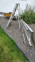 Wide view of the 5-foot step ladder standing open and the 8-foot extension ladder lying flat on gravel, showing aluminum construction and weathered condition.