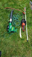 Overview photo showing Electric Weed Eater blower, hedge trimmer, and extension pruner laid out on grass