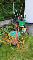 Overview photo showing Toro weed eater, extension cord, lawn aerator, hoses, seed spreader, sprinkler and edging.