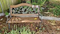 Front view of garden bench showing ornate floral metal backrest and wooden seat slats with wear and debris on ground.