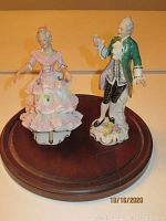 Both porcelain Dresden figurines on oval wooden base, showing man and woman figurines together