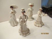 Four Lenox Victorian Lady porcelain figurines together showing full views and details such as parasol, tennis racket, and dress designs with gold trim.