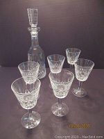 One Waterford crystal decanter with faceted stopper and six stem glasses with cut diamond patterns, displayed on dark background