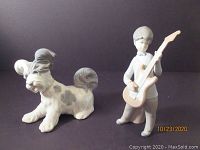 Two Lladro porcelain figurines: a small dog and a boy playing an electric guitar, displayed against a black background.