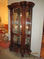 Front and side view showing the full wooden curio display cabinet with glass shelves inside and ornate carved details
