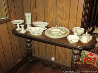 Overall view of all Lenox Holiday china pieces arranged on wooden table against wood paneling
