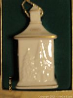 Photo of a white ceramic house holiday ornament with embossed design and gold trim inside green display box.