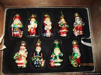 Two trays in original wooden box showing 18 different hand-painted glass Santa Claus ornaments with festive attire and various holiday accessories.