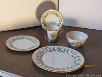 Single place setting with dinner plate, salad plate, tea cup on saucer, and bowl, showing pattern and gold trim