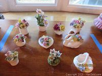 Nine small bone china floral figurines on wooden surface including swan-shaped vase and heart-shaped base floral pieces