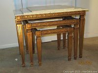 Photo showing three gilded nesting tables arranged nested, highlighting the carved apron and fluted legs.