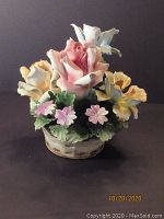 Front view of porcelain floral figurine with pastel roses, blue flowers, pink flowers, and green leaves in basket base