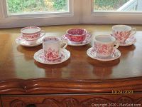 Five cranberry and white cups and saucers set displayed on wooden surface under window light.