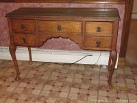 Front view of antique five drawer wooden desk with metal handles and claw-foot legs