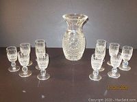 Overview of 12 Waterford Crystal cordial glasses arranged around a decanter showing full lot contents.