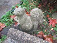 Stone squirrel statue seated on garden ground with lichen and fallen leaves
