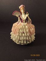 Porcelain Dresden figurine front view showing woman in pink and white dress holding fan and bird with lace skirt details.