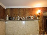 Photo showing 13 assorted steins and beer mugs arranged on a ledge, showcasing various sizes, colors, and lid types.