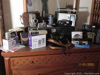 Photo of all cameras and radios arranged on wooden surface, various models and cases included