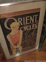 Photo of framed Orient Cycles poster featuring a woman with bicycle and text 'Orient Cycles' and 'Waltham MFG Co New York'