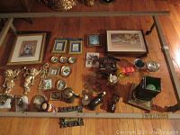 Photo showing an assortment of decorative items including small picture frames, brass figurines, a small pitcher, bookends, and other small objects spread on the floor.