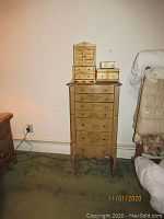 Front view of tall wooden jewelry chest with floral painted designs and multiple drawers, topped with smaller jewelry boxes.