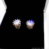 Pair of 18 karat gold plated stud earrings with clear stones displayed on black velvet inside a white jewelry box.