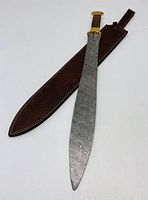 Full view of the Damascus steel blade next to its dark brown leather sheath with stitched borders.